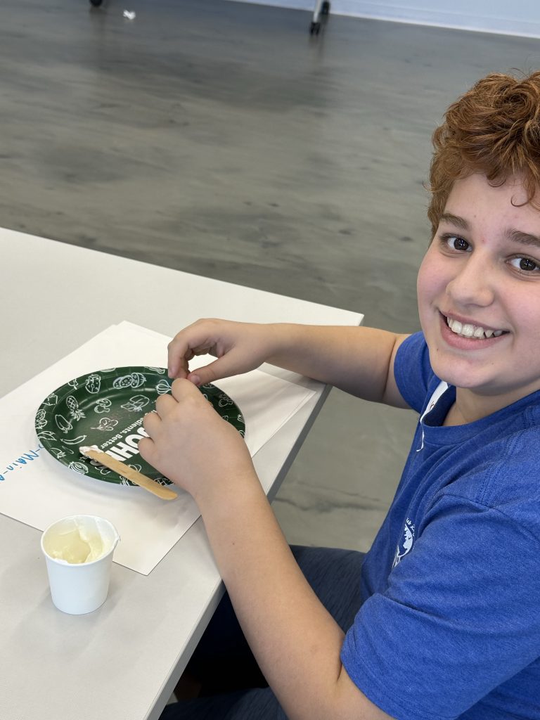 Koren is pictured during Winter Break Camp smiling in the Education Center with a paper plate and supplies to make gingerbread houses for the dogs at JHS.