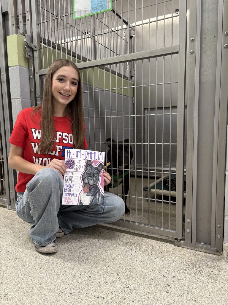 Wolfson High student Finley Hartman pictured holding an adoption poster created for Dahlia the dog by her kennel.