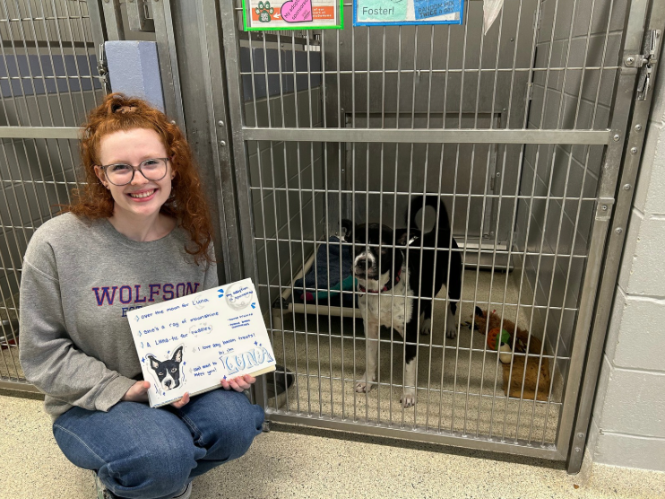 holding an adoption poster created for Luna the dog by her kennel.