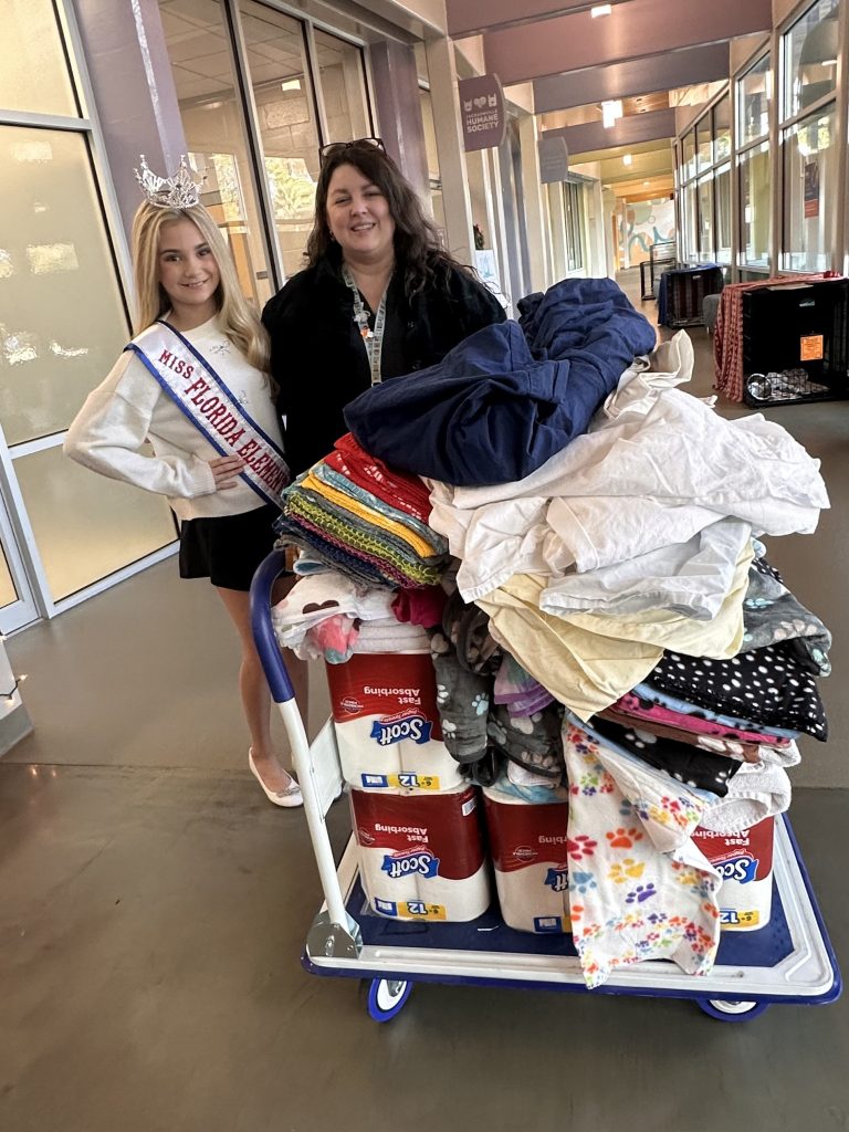 Addie posing with Ms. Savanna, the Assistant Director of Development and Education. They are both standing behind one of the carts full of donations that Addie collected. The donations include blankets, towels, and paper towels.