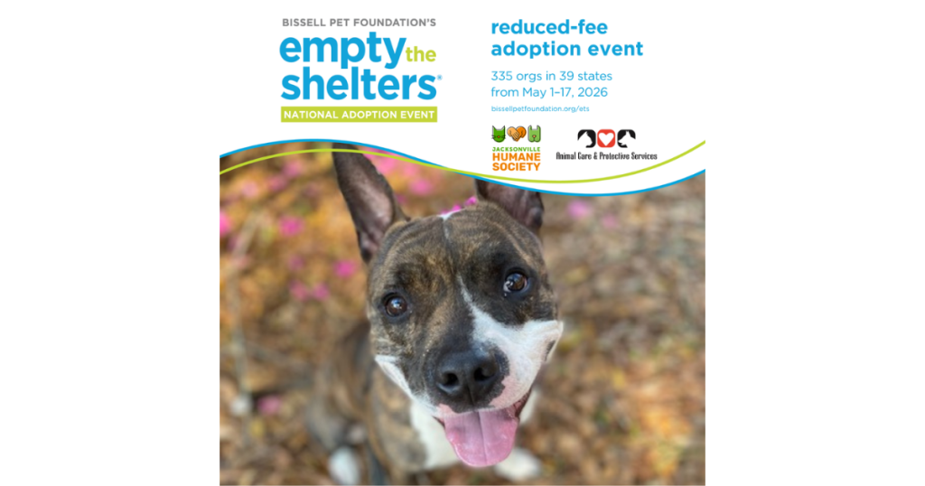 Promotional graphic for Bissell Pet Foundation’s Empty the Shelters reduced-fee adoption event. Text at the top announces the national adoption event taking place May 1–17, 2026, featuring 335 organizations in 39 states. Jacksonville Humane Society and Animal Care & Protective Services logos appear below the text. The lower portion shows a close-up photo of a happy brindle-and-white dog with upright ears and tongue out, looking up at the camera outdoors with blurred flowers and leaves in the background.
