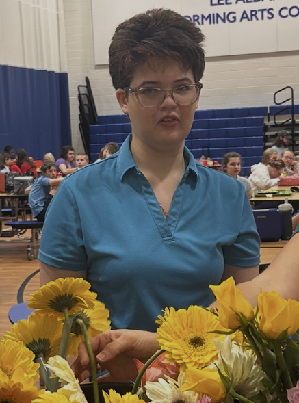 Pictured is NFSSE Senior and Treasurer of the Junior Civitan Club Megan Kennedy standing behind a set of sunflowers at the North Florida School of Special Education's gymnasium. 